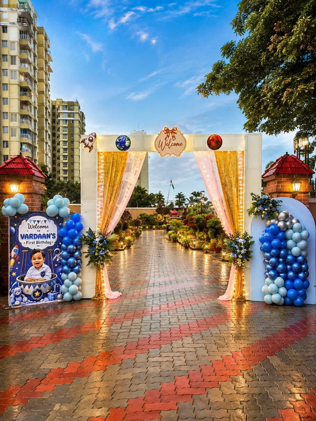 Outdoor welcome gate with gold sequin drapes, fairy lights, floral pillars and a space-themed first birthday welcome board