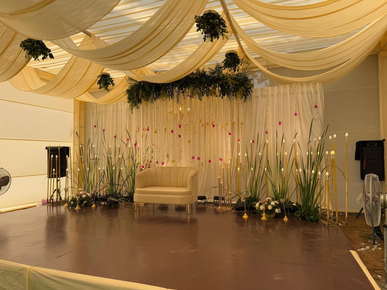Ivory draped ceremony stage with floral hanging strings and a single sofa